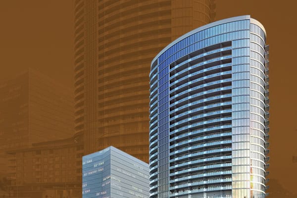 A modern, rounded glass skyscraper stands prominently in front of a darker, blurred building background under a brownish sky.