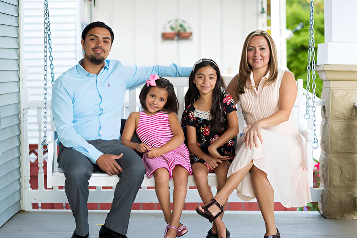 A family of four sitting on a porch swing, with two adults and two children, smiling and posing for a photo.