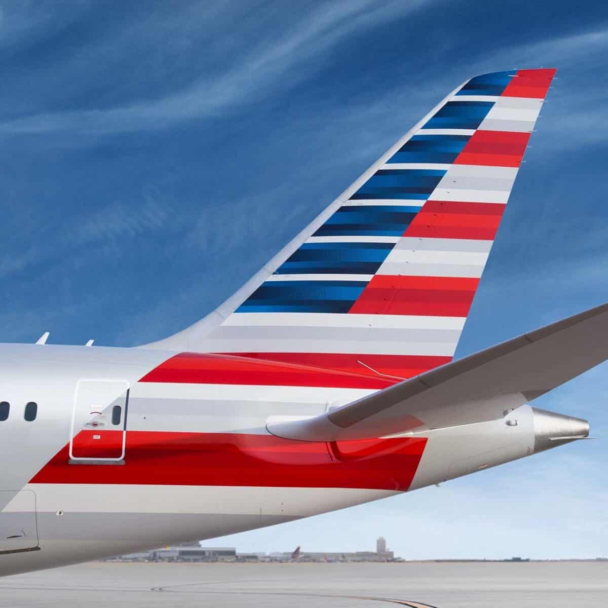 An American Airlines AAdvantage airplane tail, adorned with red, white, and blue stripes, stands proudly against a clear sky on the airport tarmac.
