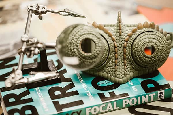 A chameleon mask and magnifying glass tool are placed on a book titled Focal Point on a table.