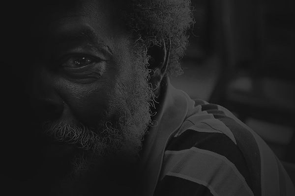 Close-up shot of an older man with a beard, partially in shadow, wearing a striped shirt. The image captures the dignity and depth often highlighted on the OurCalling nonprofit website.