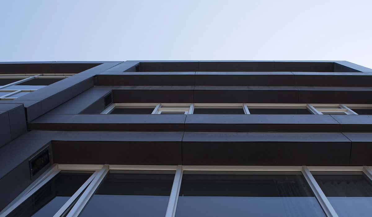 Upward view of a modern building with dark panels and large windows against a clear sky.