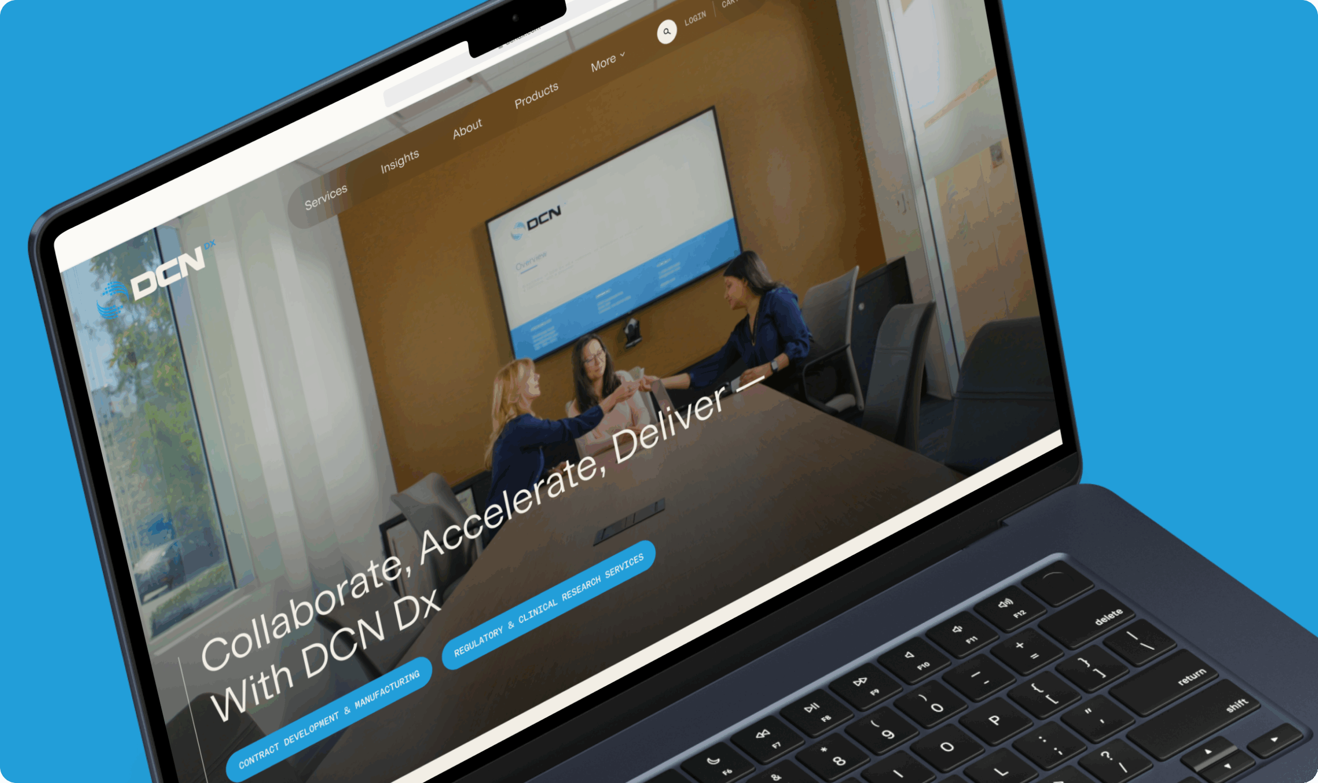 A laptop screen displays a website featuring three women in a conference room, sitting around a table and exchanging a document or item. The background wall is brown with a large screen showing the DCN logo and some text. The website header includes navigation links such as Services, Insights, About, Products, and More. The main text on the screen reads 