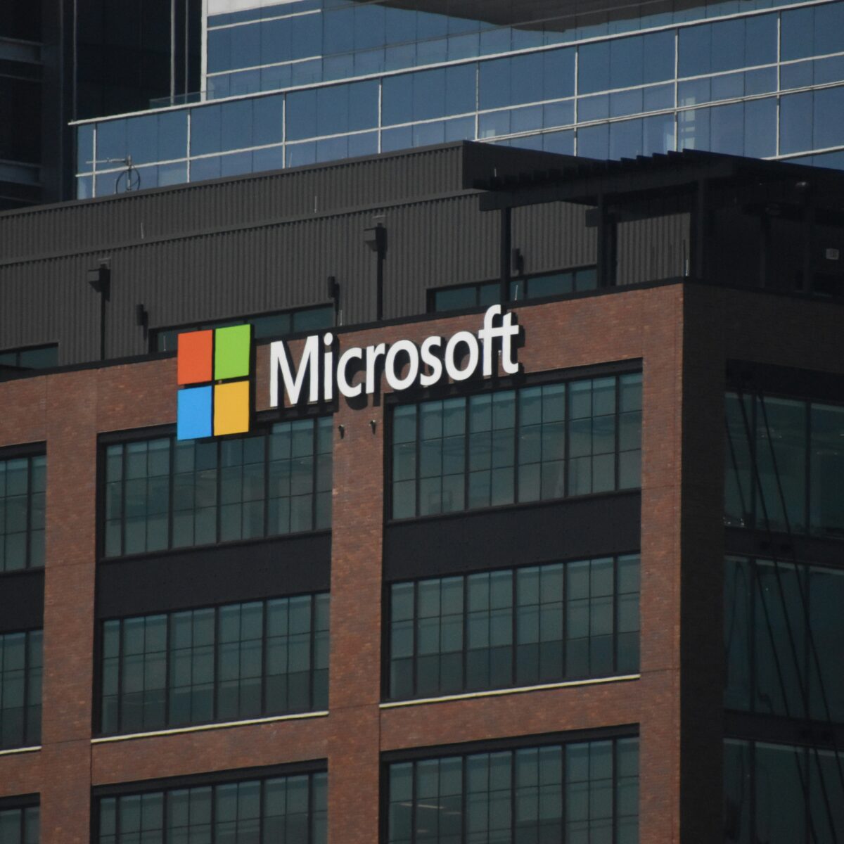 Microsoft logo with four colored squares (red, green, blue, yellow) and white text on the side of a modern brick and glass office building.